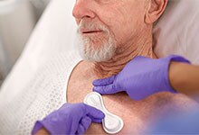 An older patient in a hospital bed has a sensor placed on his chest.