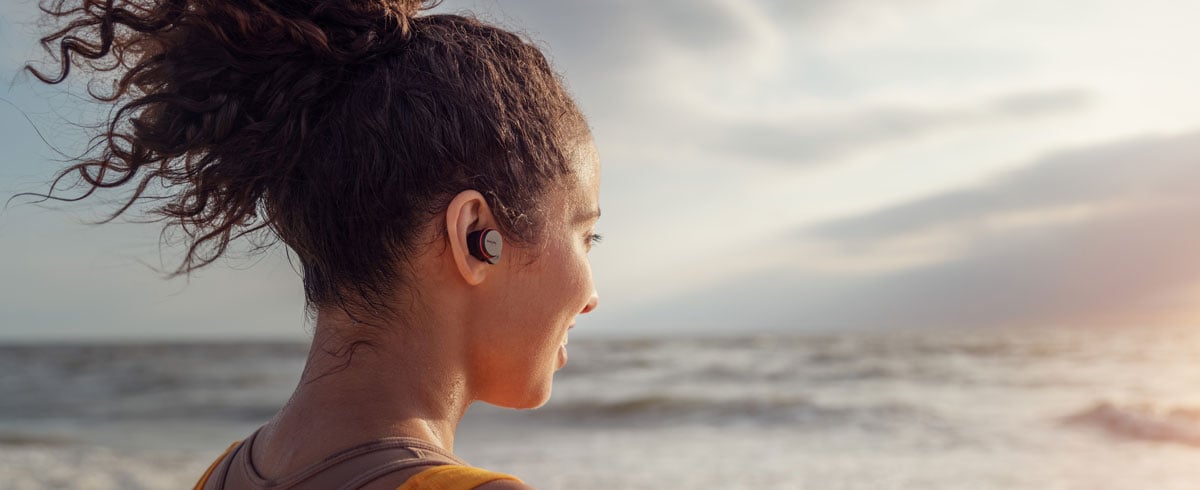 Kvinde, der bruger ægte trådløse hovedtelefoner på stranden