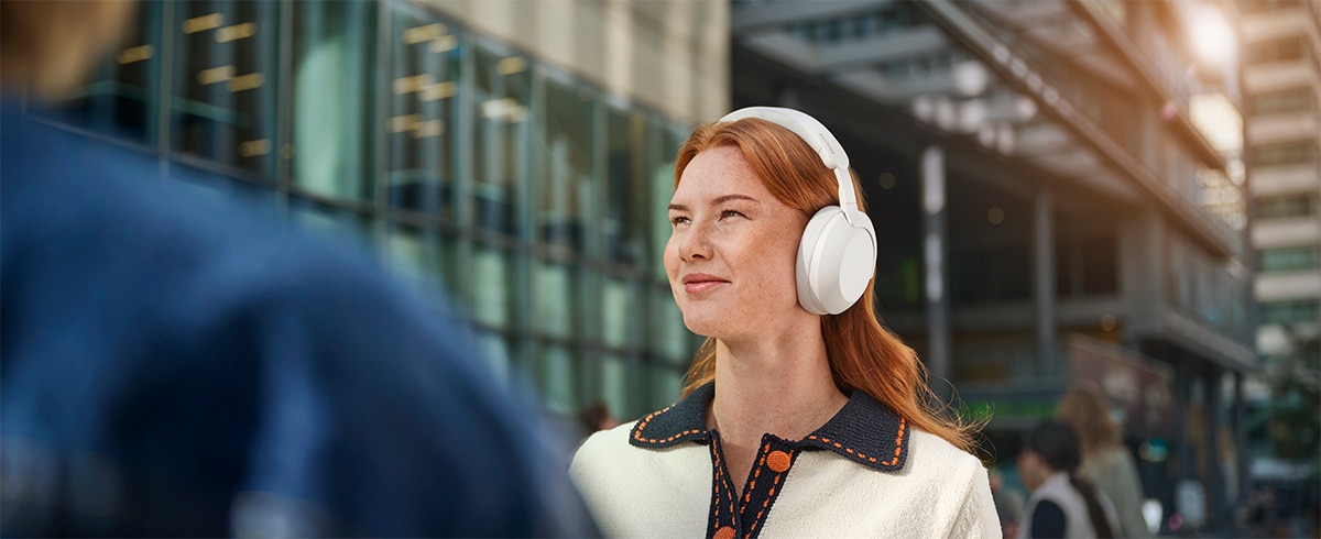 Person med Philips TAH8000EWT over-ear hovedtelefoner udendørs i et urbant miljø