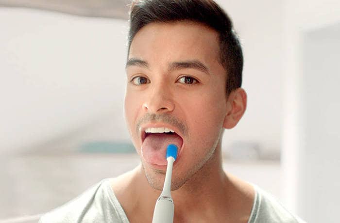En man kigger mod kameraet, mens han rengør sin tunge med en tungebørste fra Philips.