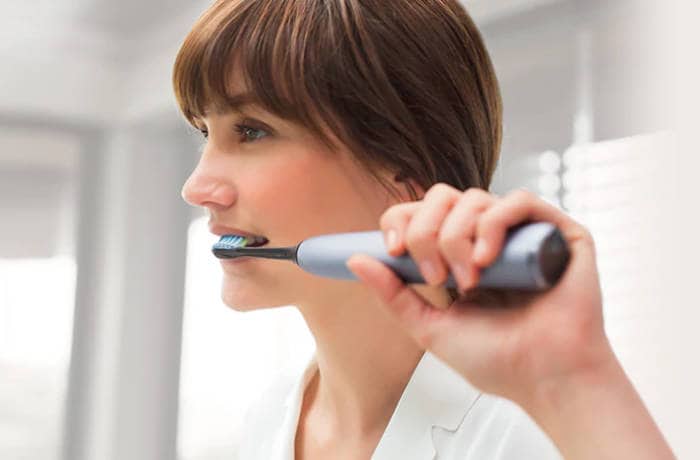 En kvinde børster tænder med en grå Philips Sonicare.