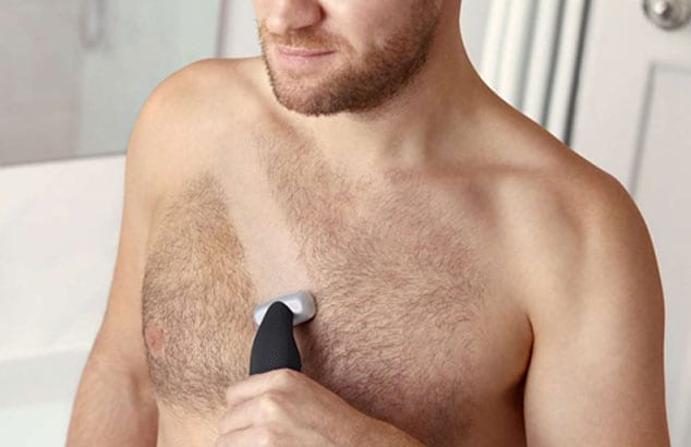 Nærbillede af en mands behårede bryst, som han er i gang med at barbere med en elektrisk skraber.