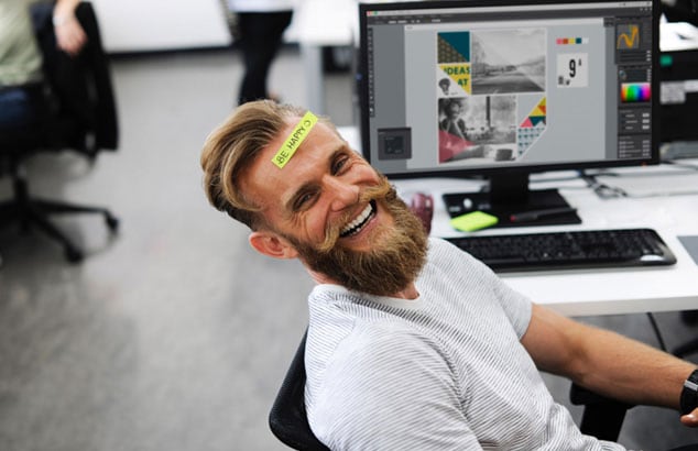 Blond, ung og grinende mand med et stort skæg sidder på en kontorstil og smiler til kameraet