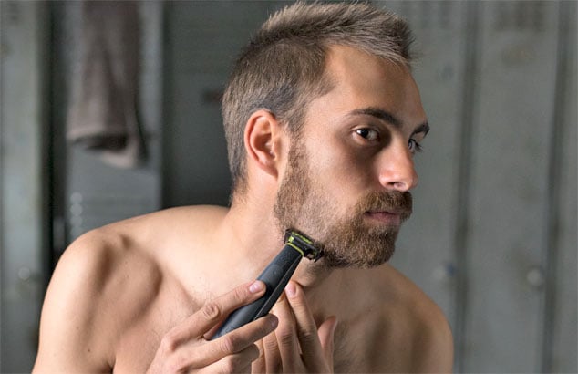 En mand trimmer sit utæmmede skæg ned til skægstubbe med en trimmer med tilbehør. 