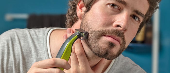 En mand barberer let sit skæg med en trimmer med tilbehør.
