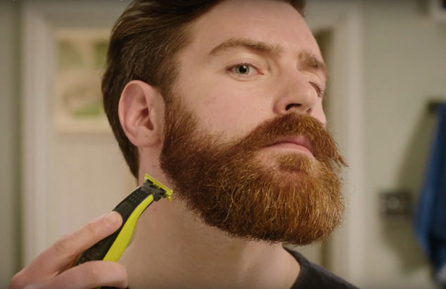 En mand trimmer sit vilde skæg ned til stubbe med en trimmer med særligt tilbehør.