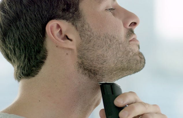 En mand i profil med et kort skæg, som barberer sin hals med en elektrisk skraber.