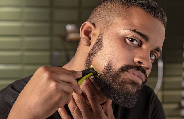 En mand barberer sit korte skæg i en nedadgående retning fra sin kind til sin kæbelinje, hvilket resulterer i et glatbarberet område af hans kind. 