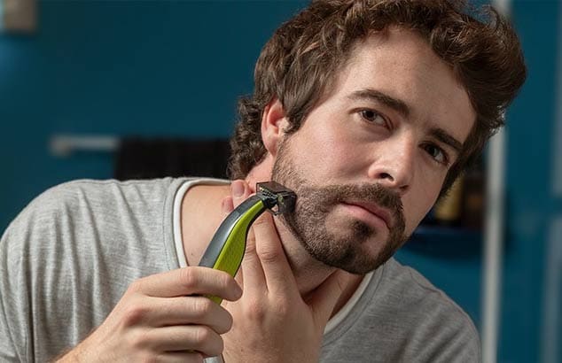 En ung mand er i gang med at bruge en trimmer med et særligt vedhæng til at trimme et utæmmet skæg med. 