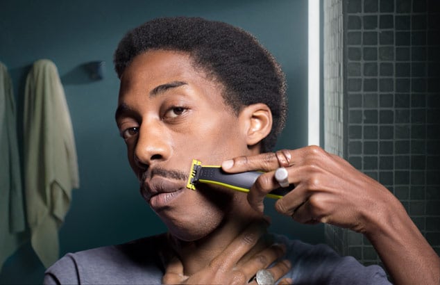 En ung mand trimmer sit overskæg med en Philips OneBlade foran et spejl på et badeværelse