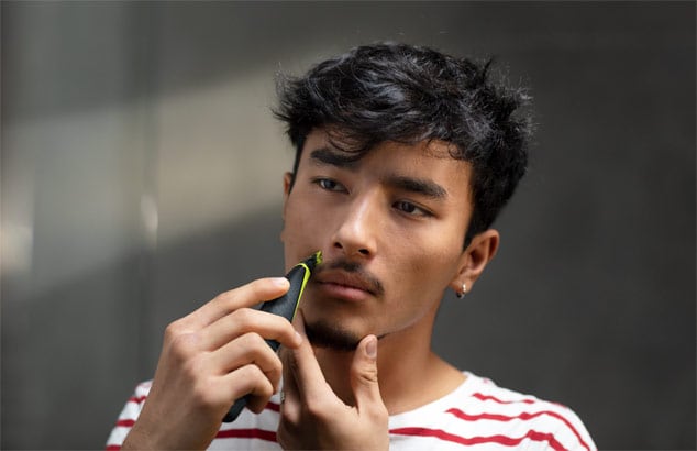 En ung mand i en rød- og hvidstribet T-shirt trimmer sit overskæg med en Philips OneBlade