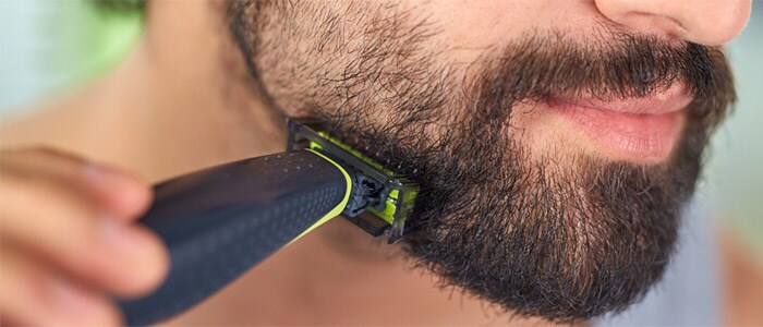 Nærbillede af en mand med brune øjne, som er i gang med at barbere og trimme sit mørke skæg med en Philips OneBlade