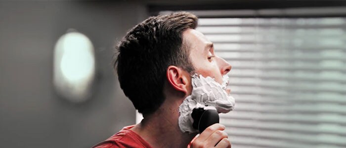 En mand med barberskum i ansigtet barberer sig med en elektrisk skraber.